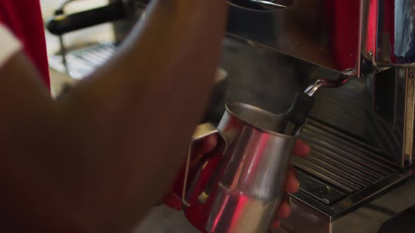 Midsection of african american barista using coffee machine frothing milk in cafe