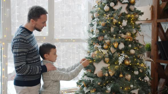 Father and Son Decorating New Year Tree Hanging Bright Balls and Talking at Home