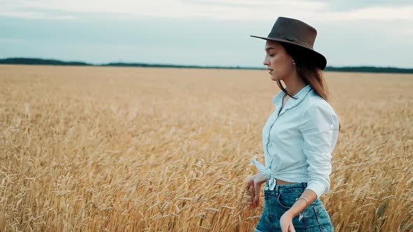 Young Girl in Shorts and Hat Walking Down the Wheat Fields, Smiling in the Camera and Touching the