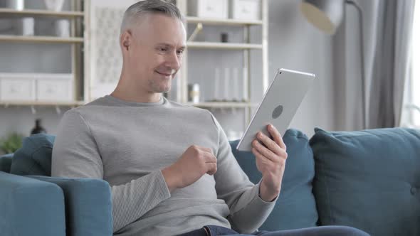 Online Video Chat on Tablet By Gray Hair Man Relaxing on Couch