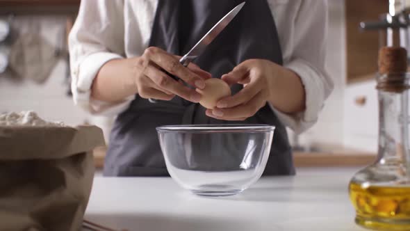 Female Hands Break An Egg With A Knife. A Woman Breaks An Egg Into A Glass Bowl. The Process