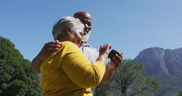 Happy senior african american couple using smartphone taking selfie in sunny garden