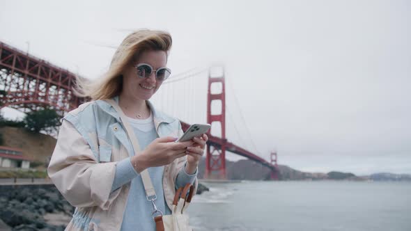 Happy Caucasian Woman Holding Cell Phone Using Smartphone Outdoor at Golden Gate