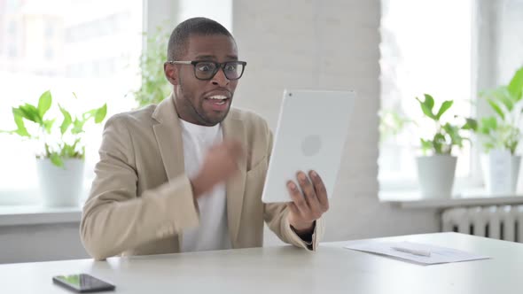 African Man Celebrating Success on Tablet in Office