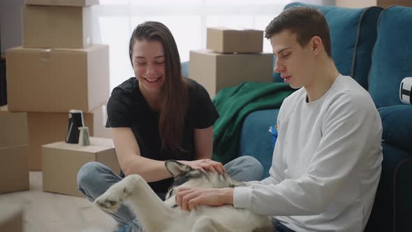 Happy Young Man and Woman Sitting on the Floor in a New Apartment with Cardboard Boxes Laughing and