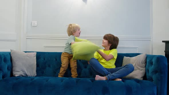 Two Kids Fight with Pillows Sitting on the Couch at Home