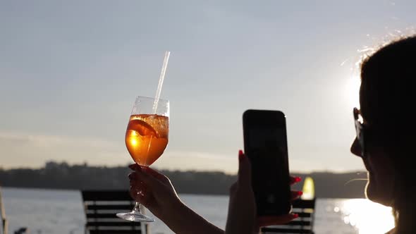 Female Blogger Takes Pictures of a Glass of Cocktail in a Cafe with Her Phone