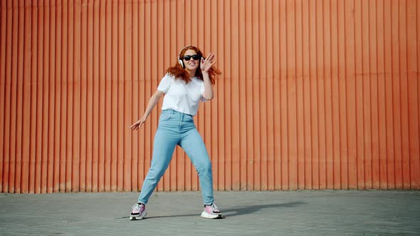 Joyful Young Lady Dancing Outdoors Wearing Headphones and Sunglasses