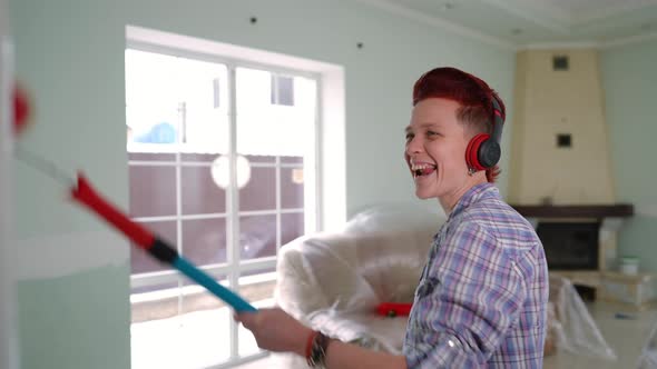 Side View Cheerful Woman in Headphones Dancing Listening to Music Painting Wall in New House