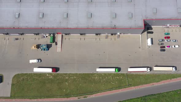 Moving Aerial Side Shot of Industrial Warehouse Loading Dock where Many Truck with Semi Trailers Loa