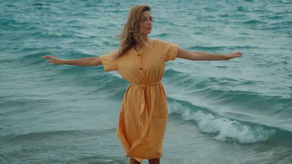 A Slim Blonde in a Yellow Dress Walks Along the Beach and Looks Around