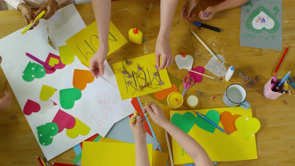 Top View of Hands of Kids Putting Flowers on Greeting Card for Mom alt