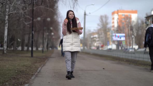 Pretty Woman Walking Outdoors in the City and Eating Burger