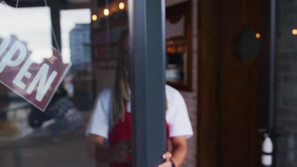 Mixed race male barista with dreadlocks closing the door and switching the sign from open to closed