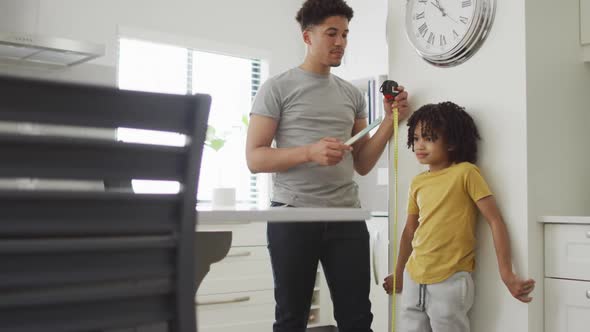 Happy biracial man and his son measure height in kitchen