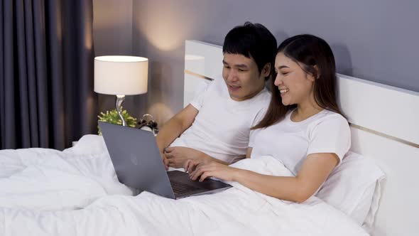 couple using laptop together on a bed