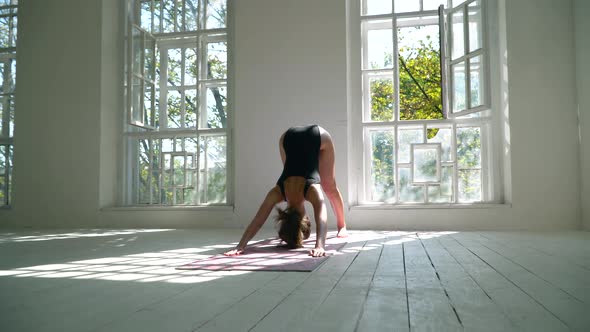 Red-haired Young Healthy Caucasian Woman Standing on the Mat in the White Large Room Practicing Yoga