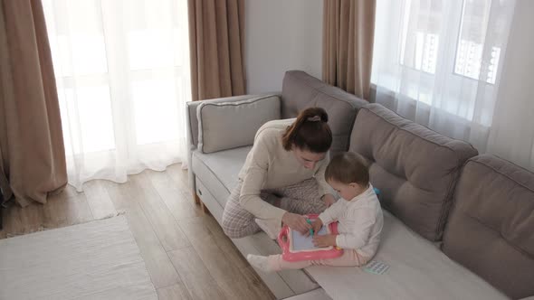 Caring Young Mother or Nanny Helping Her Cute Daughter Teach the Baby Draw a Picture with Pencils