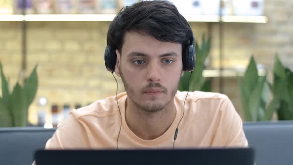 Closeup Portrait of Absorbed Handsome Caucasian Young Man in Headphones Surfing Internet on Laptop