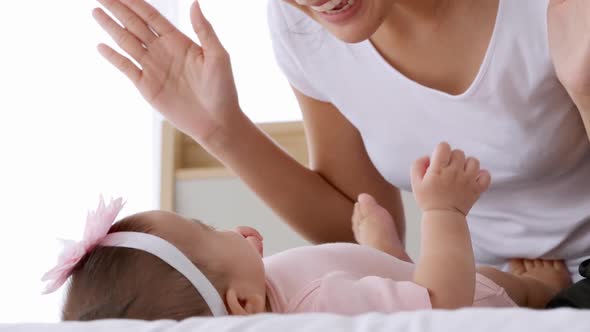 Young mother with her little baby playing on bed at home.