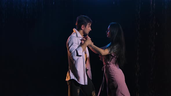 Loving Couple Passionately Dances Against the Background of the Rain in a Dark Studio