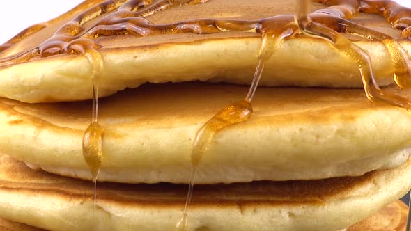 American pancakes with maple syrup on a white background. Pancake lies on a black slate round stone.