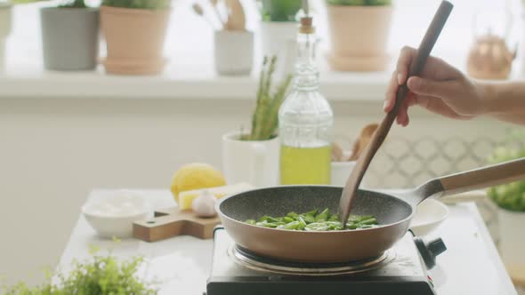Unrecognizable cook frying green beans in pan