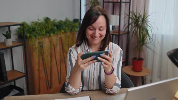 Worried Young Business Woman Enthusiastically Playing Racing or Shooter Video Games on Smartphone