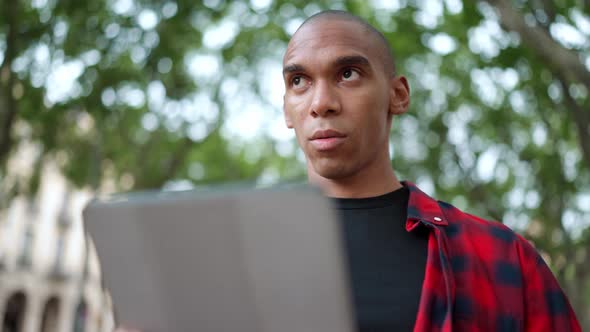 Pensive bald African man typing on digital tablet on the bench