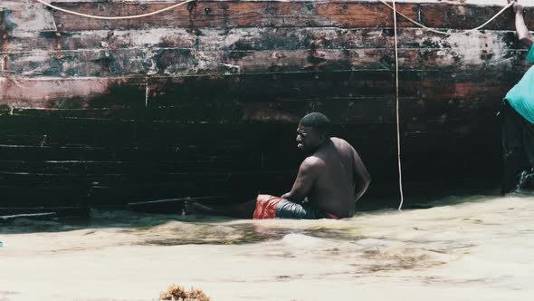 An African Fisherman Cleans a Boat From Algae on the Shore at Low Tide Zanzibar