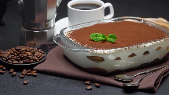 Tiramisu Dessert in Glass Baking Dish, Cup of Espresso and Coffee Maker on Concrete Background