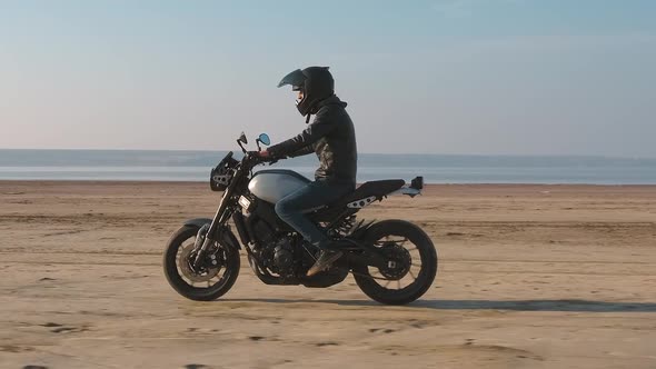 Motorcyclist Driving His Customized Fast Motorbike on the Dirt Road in Desert Around Sea or Lake