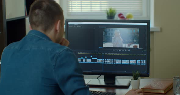 Male Video Editor Works with Footage and Sound on His Personal Computer. His Office Is Modern and