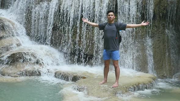 Man Standing With Raised Hands at Waterfall