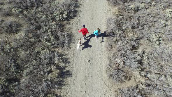 Aerial shot of a young man and woman trail running with dog on scenic mountain trail.