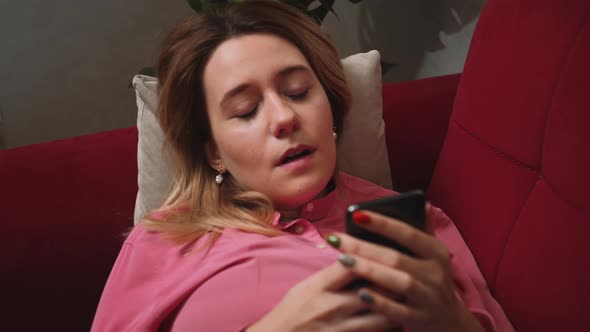Close Up Relaxed Woman Hold Use Smartphone Watching Social Media Yawning on the Couch Sofa at Home