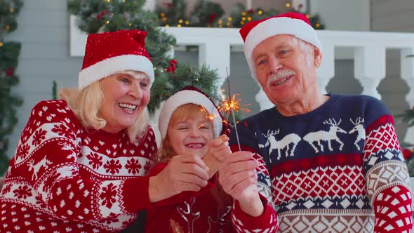 Happy Senior Couple Grandparents with Granddaughter Holding Lit Bengal Christmas Lights Sparklers