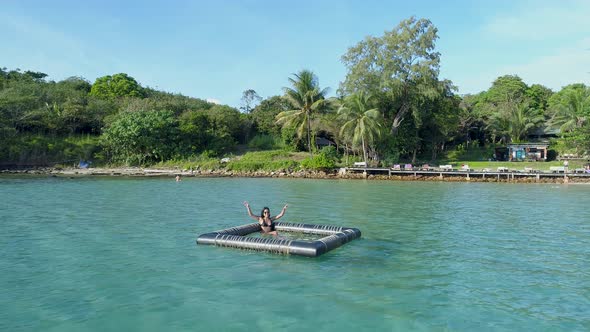 Girl sitting and waving in a inflatable floating device in the ocean, Koh Kood, Thailand