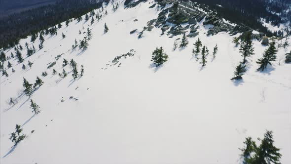 Drone flies over mountain ridge, blue cloudy sky and snow covered slopes