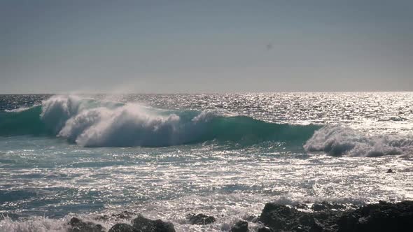 Slow motion view of clear turquoise sea and waves breaking against the rocky shoreline of the Teneri