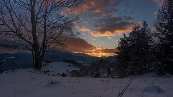 idyllic sunset in a snowy landscape with moving colorful clouds, trees and a snowman