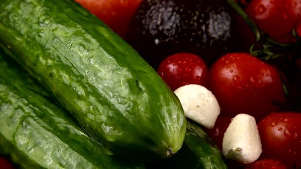 Cherry tomatoes, cucumbers, garlic, avocado and red onion on a black background in water drops