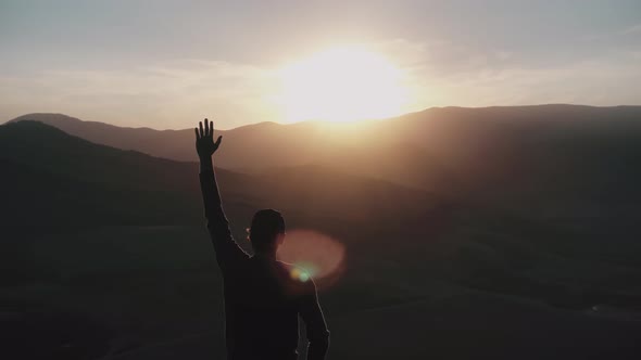 A Young Man Stands in the Rays of the Sunset and Pulls His Hand Up Aerial Survey of a Drone Which