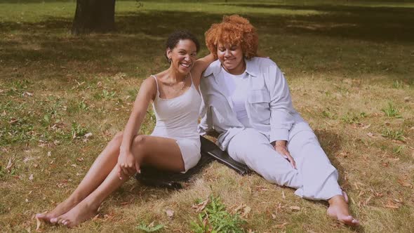 Lovely Beautiful Happy Lesbian African American Couple Sitting on Green Grass Hugging Outside at