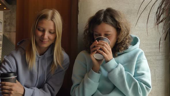 Women in Hoodies Drink Coffee and Talk Near Dracaena in Cafe