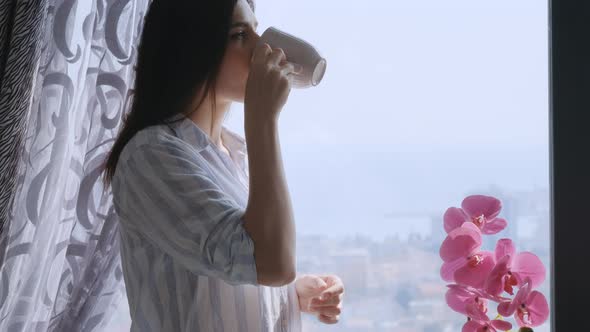 Camera slowly moves up brunette  woman drinking coffee and looking at window