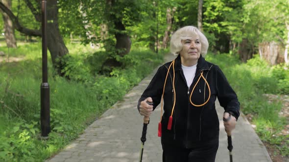 Active Senior Old Woman Training Nordic Walking with Ski Trekking Poles in Park