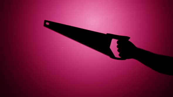 Man Holding Saw Closeup Shadow Silhouette of Hand with Sharp Tool on Pink Neon Background