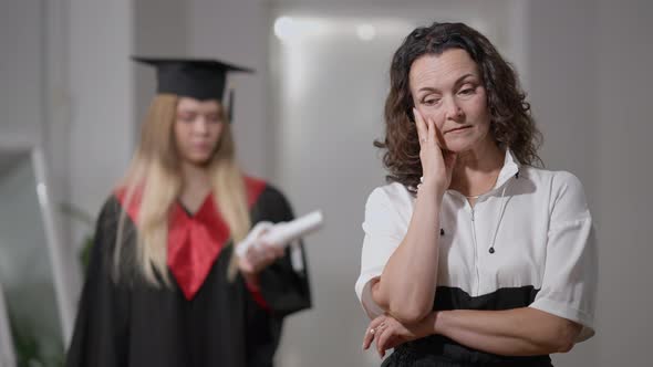 Portrait of Stressed Caucasian Sad Mother Standing at Home with Blurred Graduate Daughter at