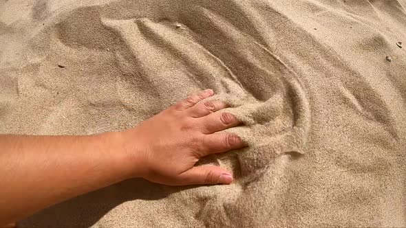Person Runs His Hand Over Surface of Yellow Sand Scatters It with Fingers